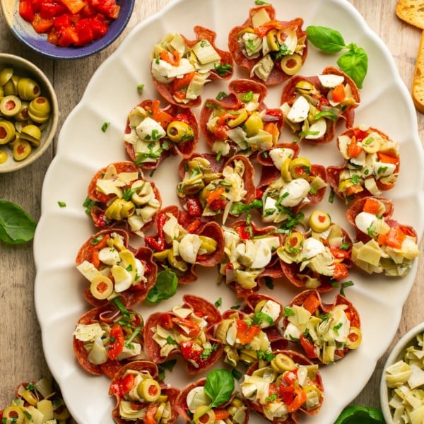 white plate with salami cups stuffed with artichokes olives cheese and roasted peppers