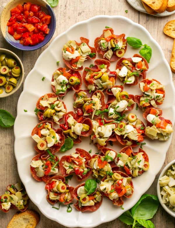 white plate with salami cups stuffed with artichokes olives cheese and roasted peppers