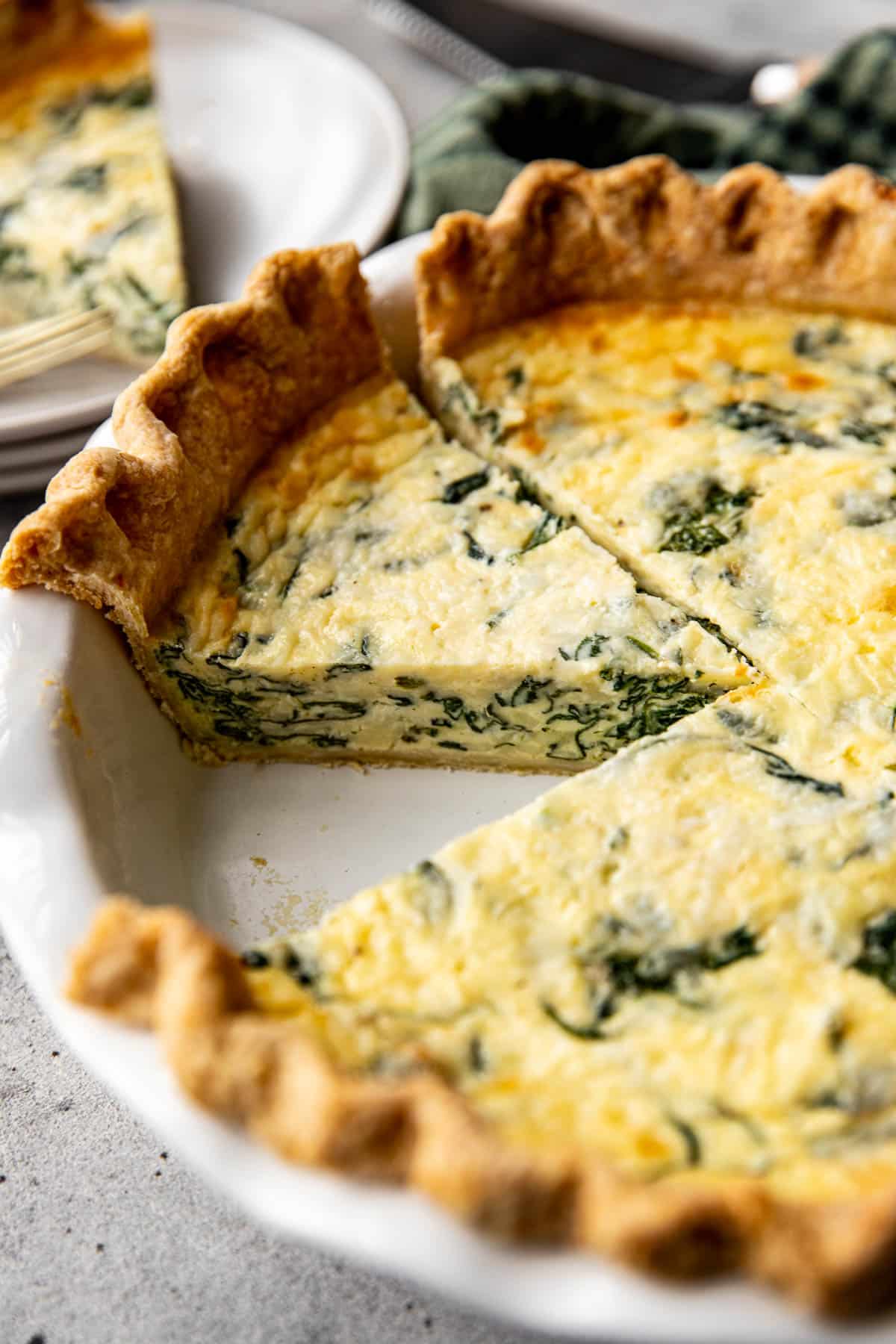 a slice of quiche in a white pie plate. 