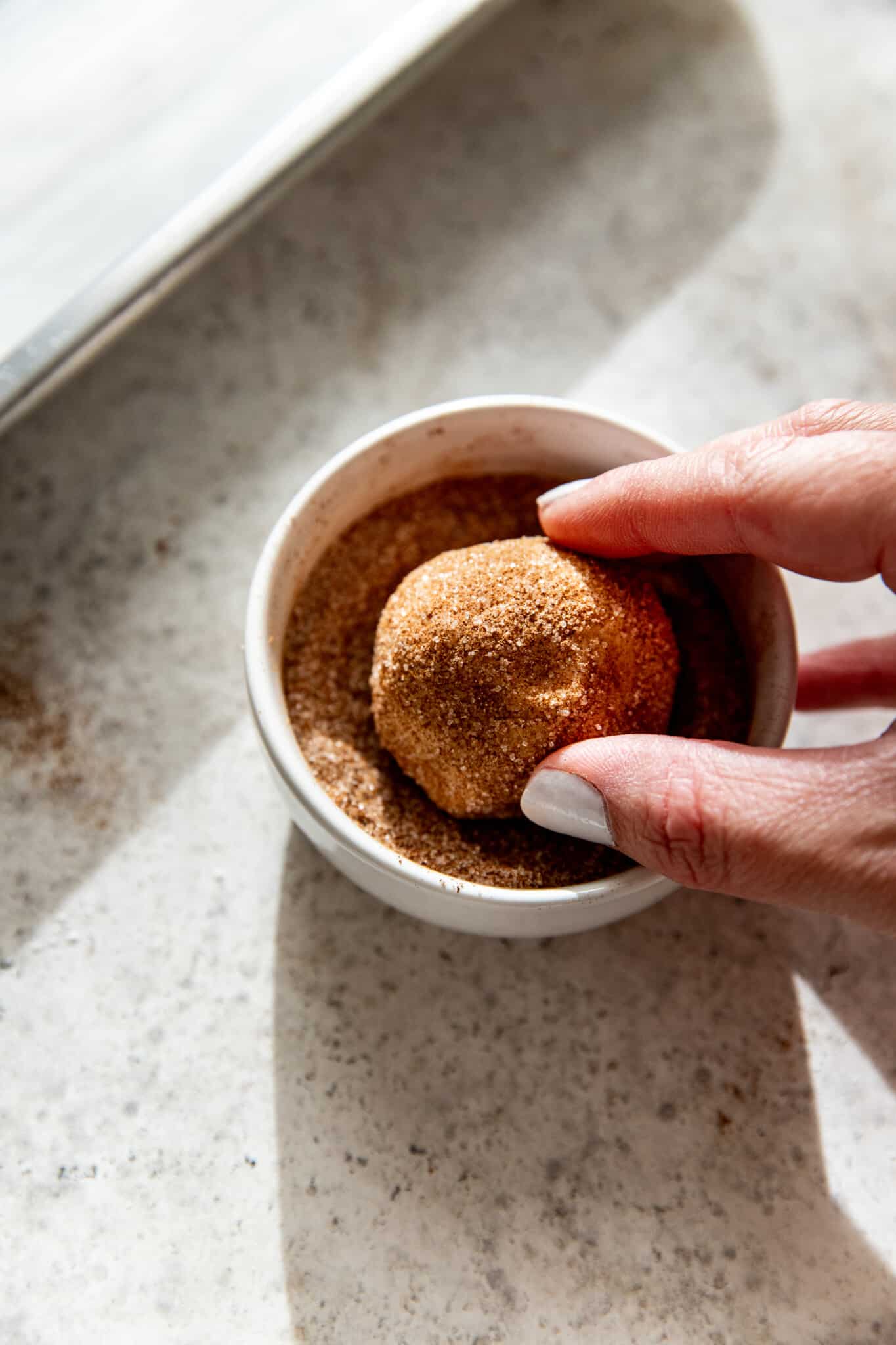 a womans. hand rolling snickerdoodle cookie dough in cinnamon and sugar. 