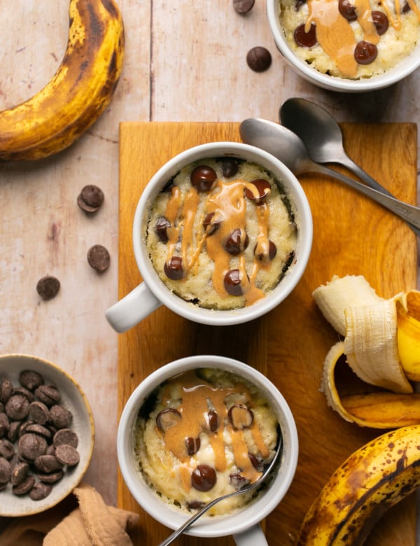 banana mug cake in a white ceramic mug topped with peanut butter and chocolate chips.