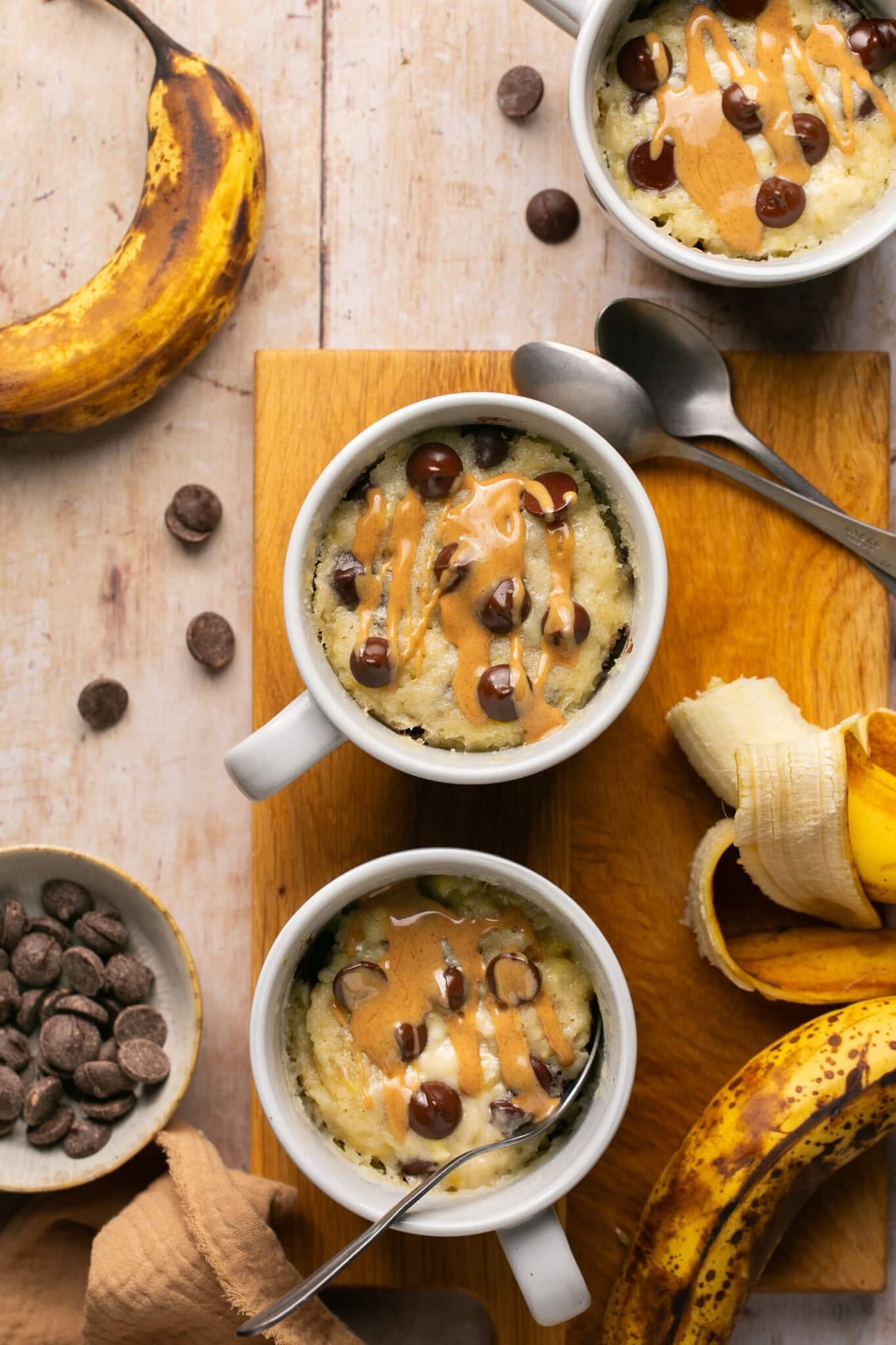 banana mug cake in a white ceramic mug topped with peanut butter and chocolate chips.