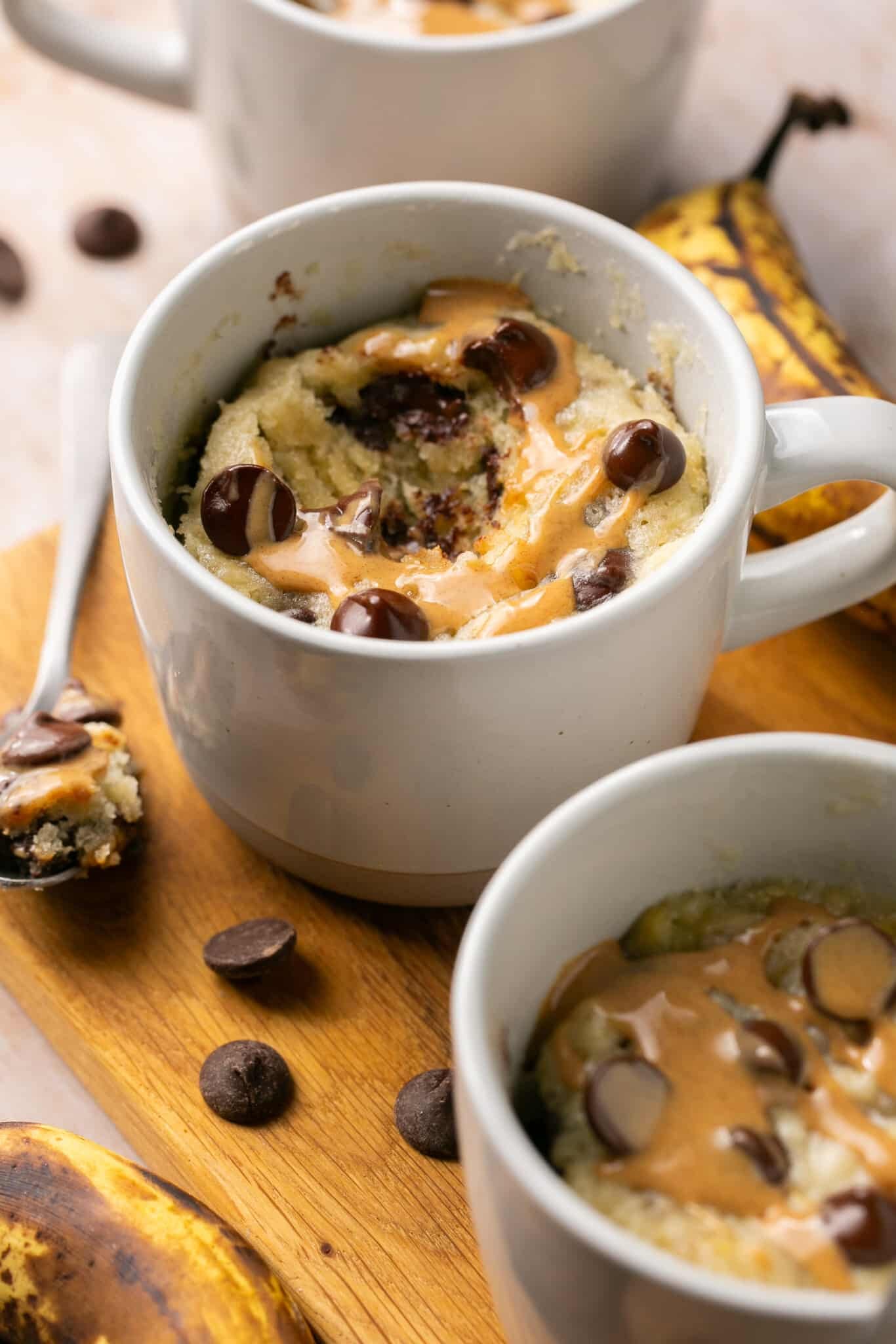 a cooked mug cake in a white mug with chocolate chips and peanut butter drizzled on top.