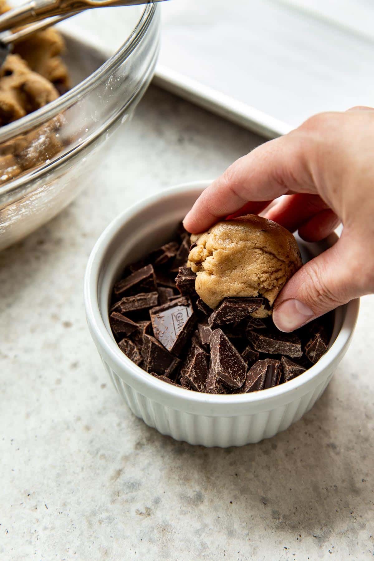 a womans hand dunking a cookie dough ball into chocolate chunks. 