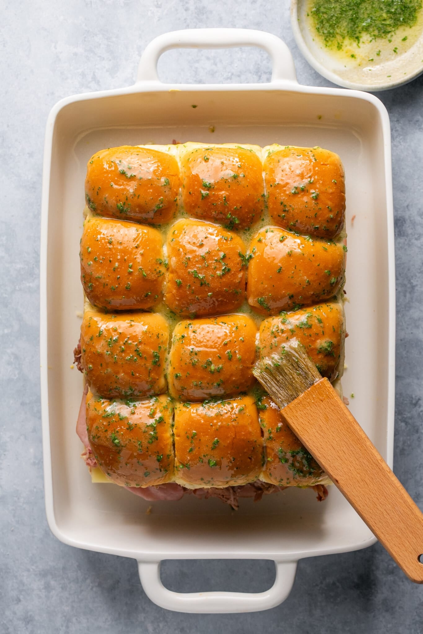 butter and parsley being brushed on slider rolls. 