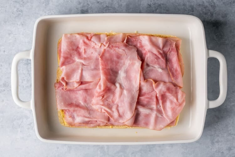 ham slices on dinner rolls in a white baking dish.