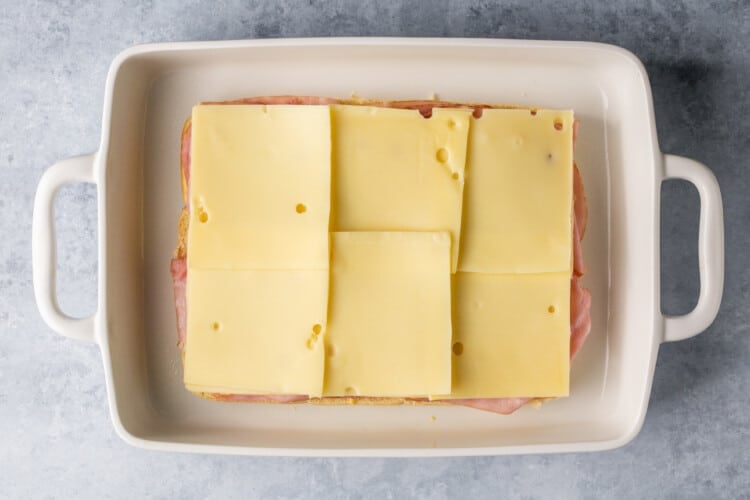 swiss cheese on top of ham on dinner rolls in a white baking dish.