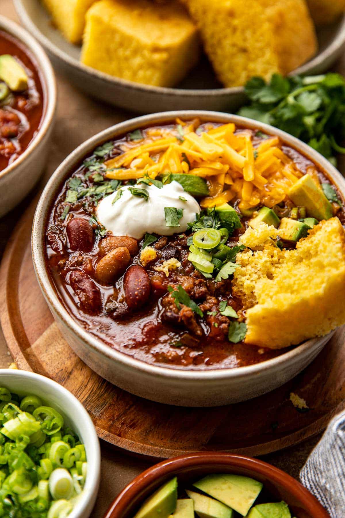 chili in a bowl with cornbread, sour cream, avocado and cheese. 