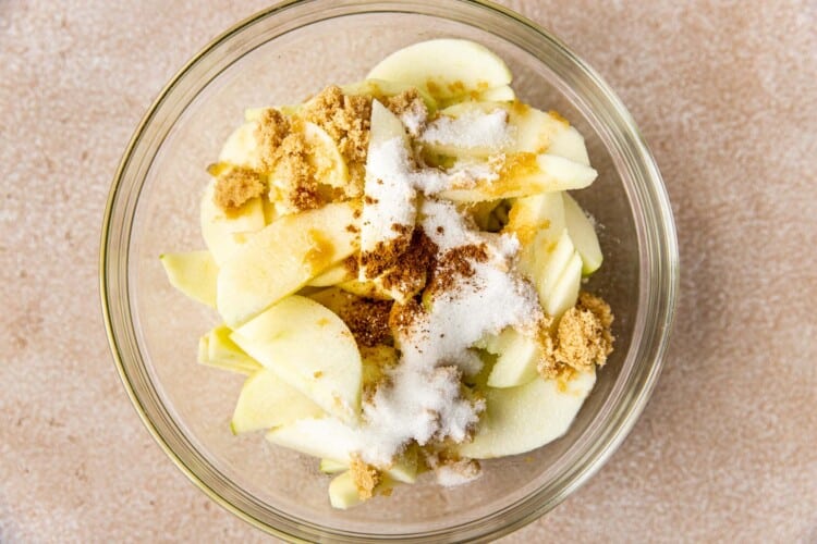 apples in a glass mixing bowl with spices and sugar.