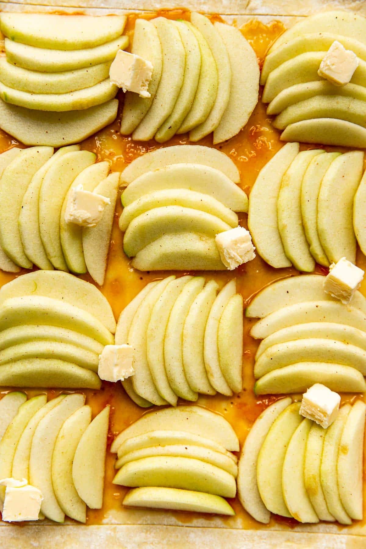 a close up image of apples on puff pastry with butter dotted on top.