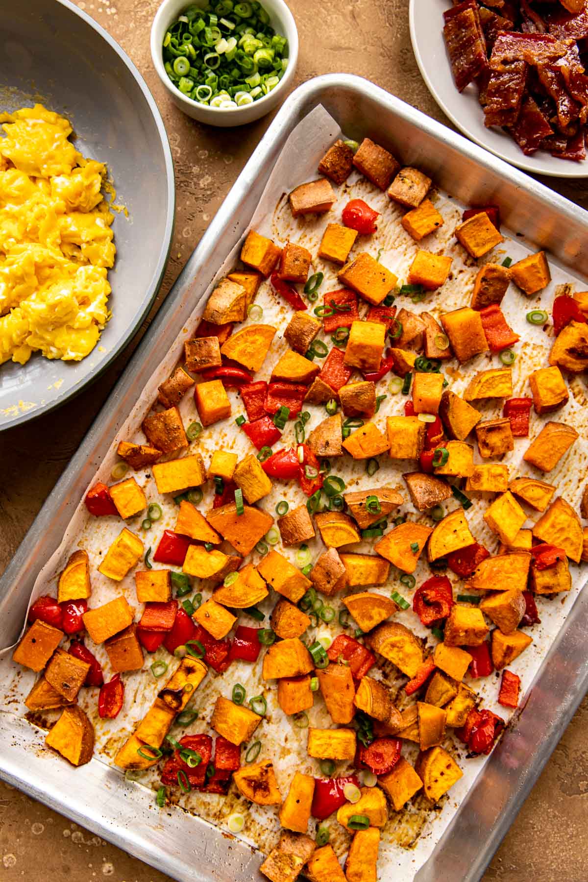 roasted sweet potatoes and red bell peppers on a baking sheet garnished with green onions. 