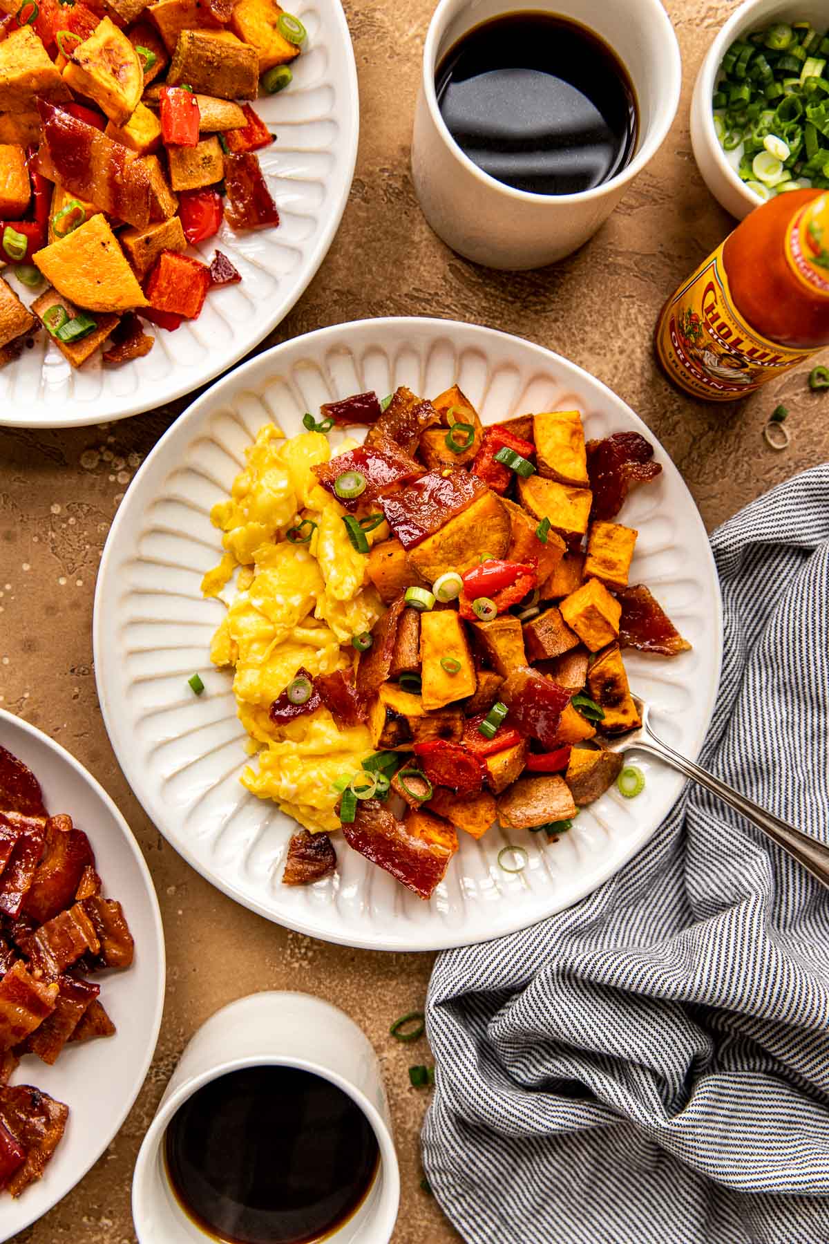 scrambled eggs, sweet potatoes, candied bacon on a white plate garnished with green onions. 