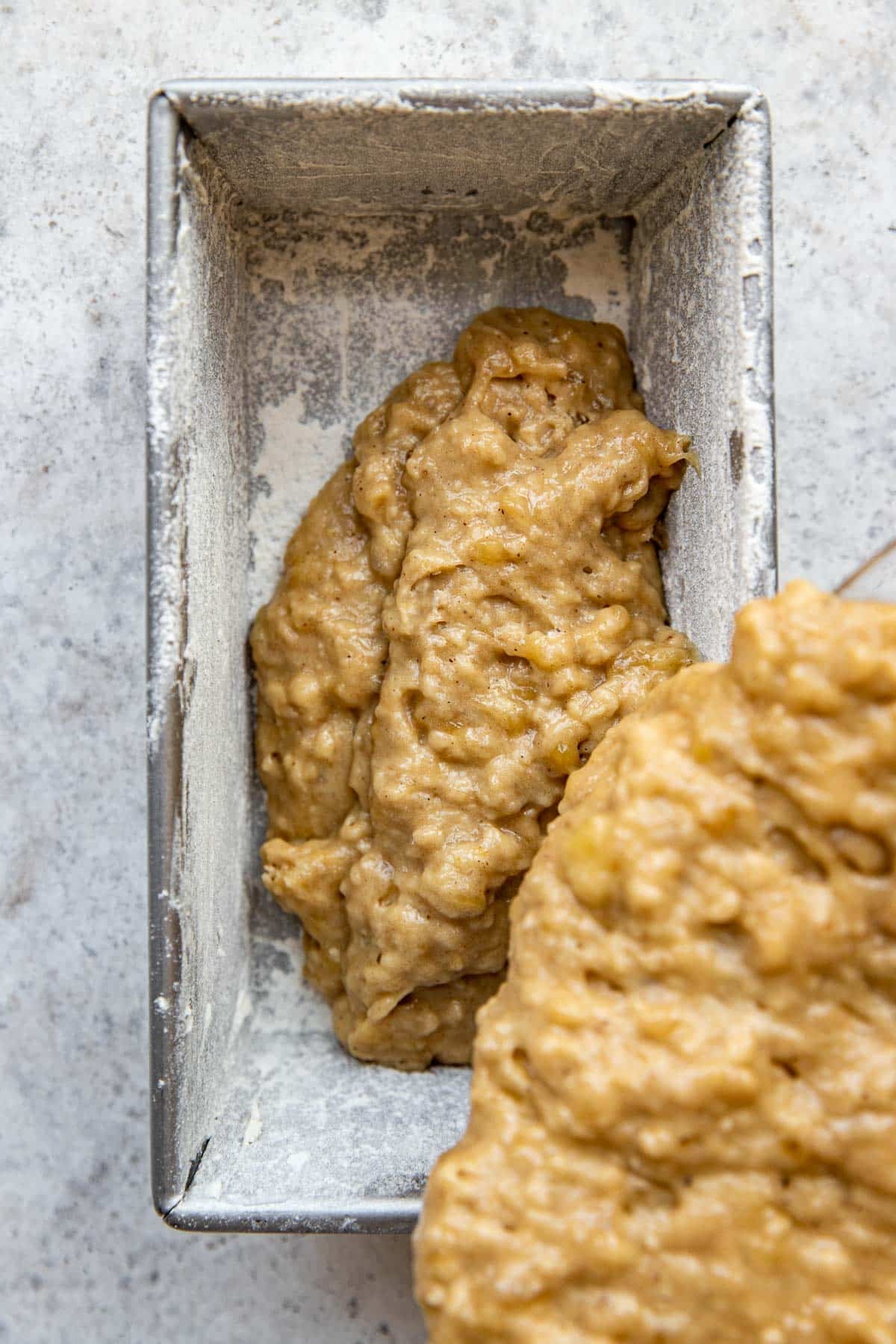 banana bread batter being poured into a loaf pan. 