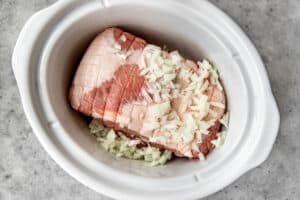 pulled pork butt in a white crock pot with onions on top.