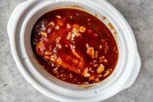sauce and onions poured over a pork shoulder in a white slow cooker.