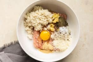 Ingredients to make chicken meatballs in a large white mixing bowl.