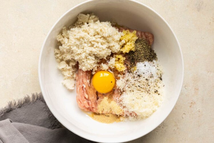 Ingredients to make chicken meatballs in a large white mixing bowl.