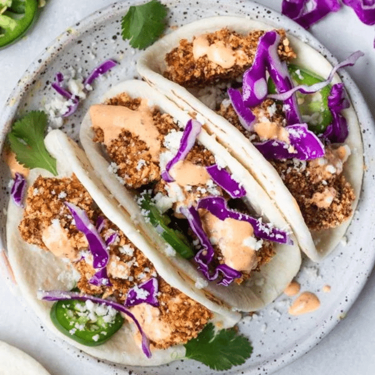 three tacos with crusted mahi mahi fish, cabbage, sauce, and jalapenos