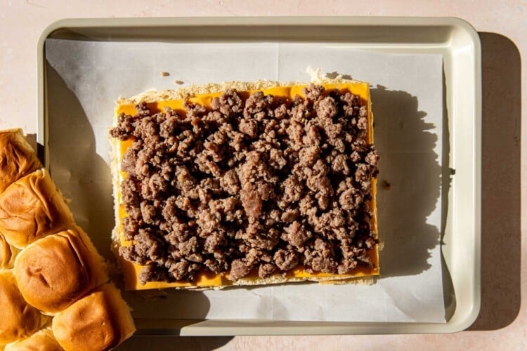 rolls with sausage and cheese on top on a parchment paper lined baking sheet.