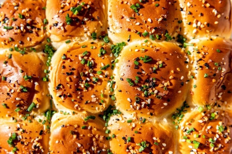 breakfast sliders on a parchment paper lined baking sheet garnished with chives and everything but the bagel seasoning.