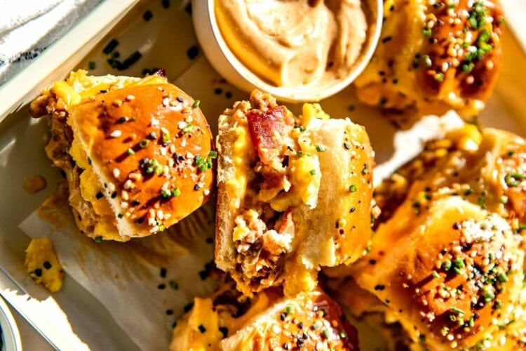 breakfast sliders on a parchment paper lined baking sheet garnished with chives and everything but the bagel seasoning.