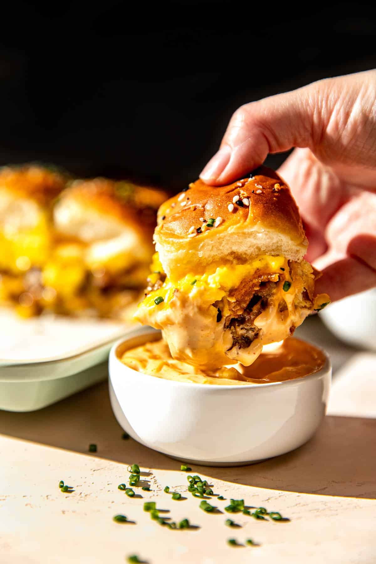 a womans hand holding a breakfast sandwich dunking it in sriracha mayo. 