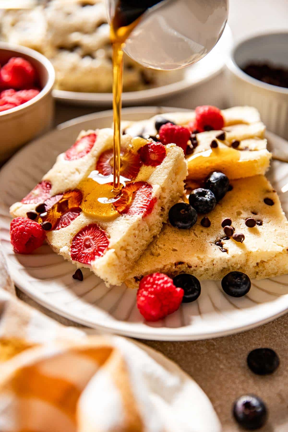 syrup being poured onto pancakes on a white plate.