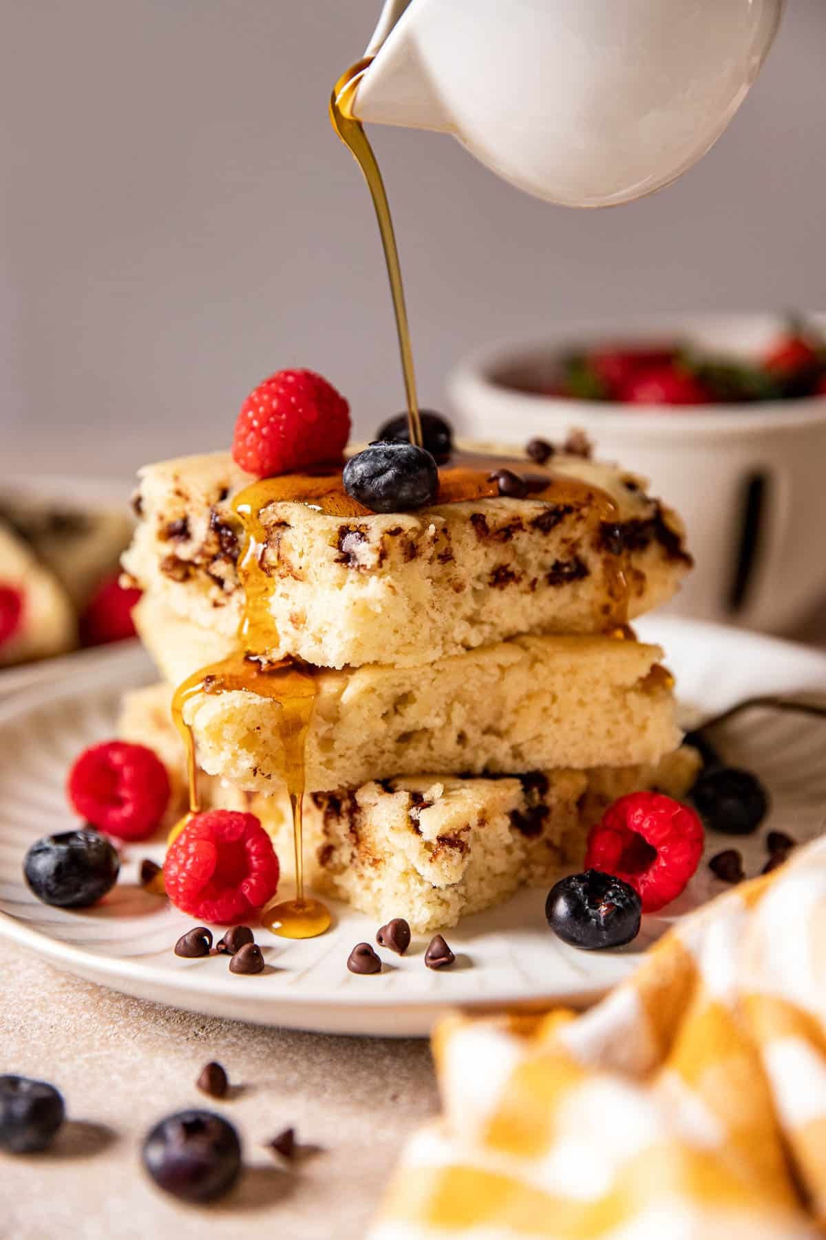 pancakes on a white plate with fresh berries and syrup poured on top. 