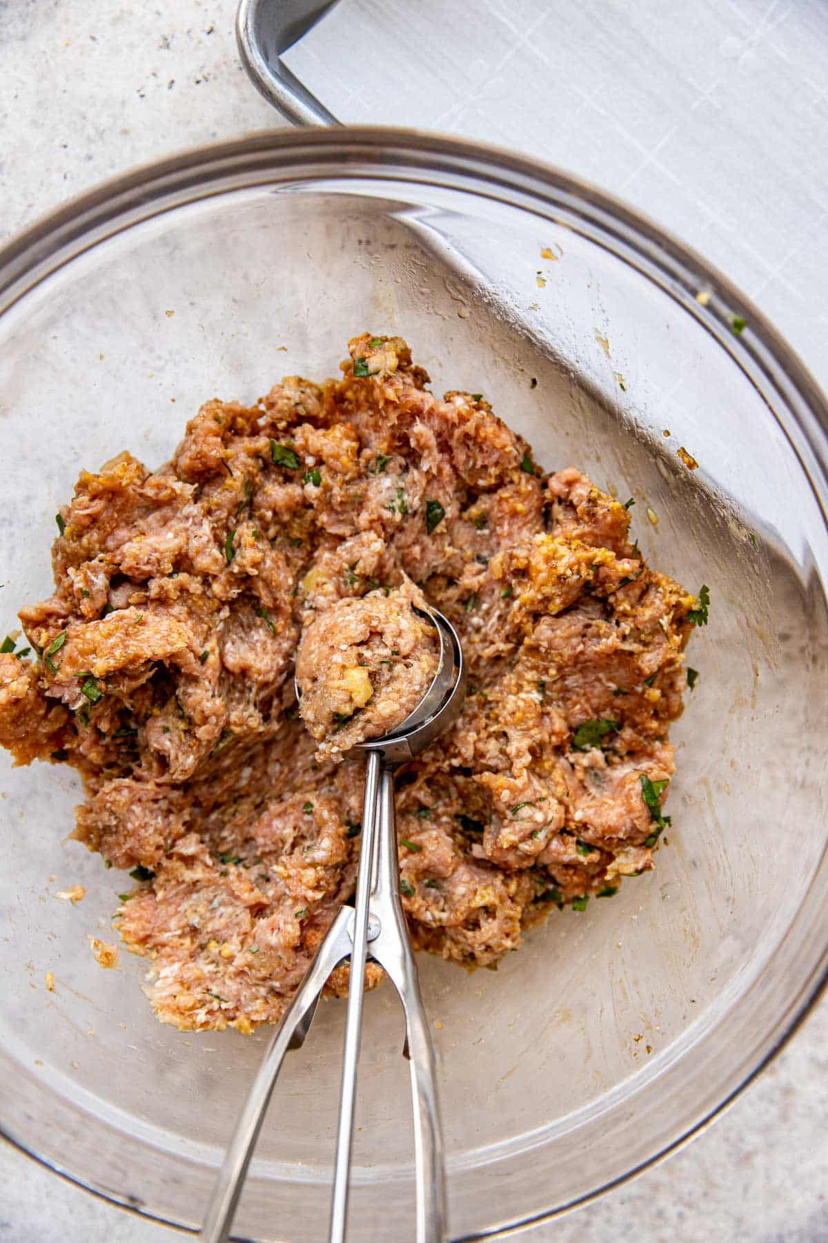 ground turkey meatball mixture in a glass bowl with a cookie scoop. 