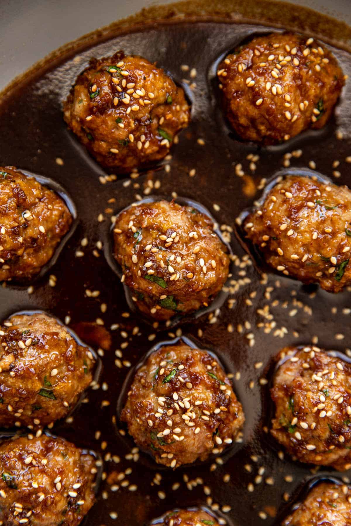 an up close image of meatballs in a sauce with sesame seeds on top. 