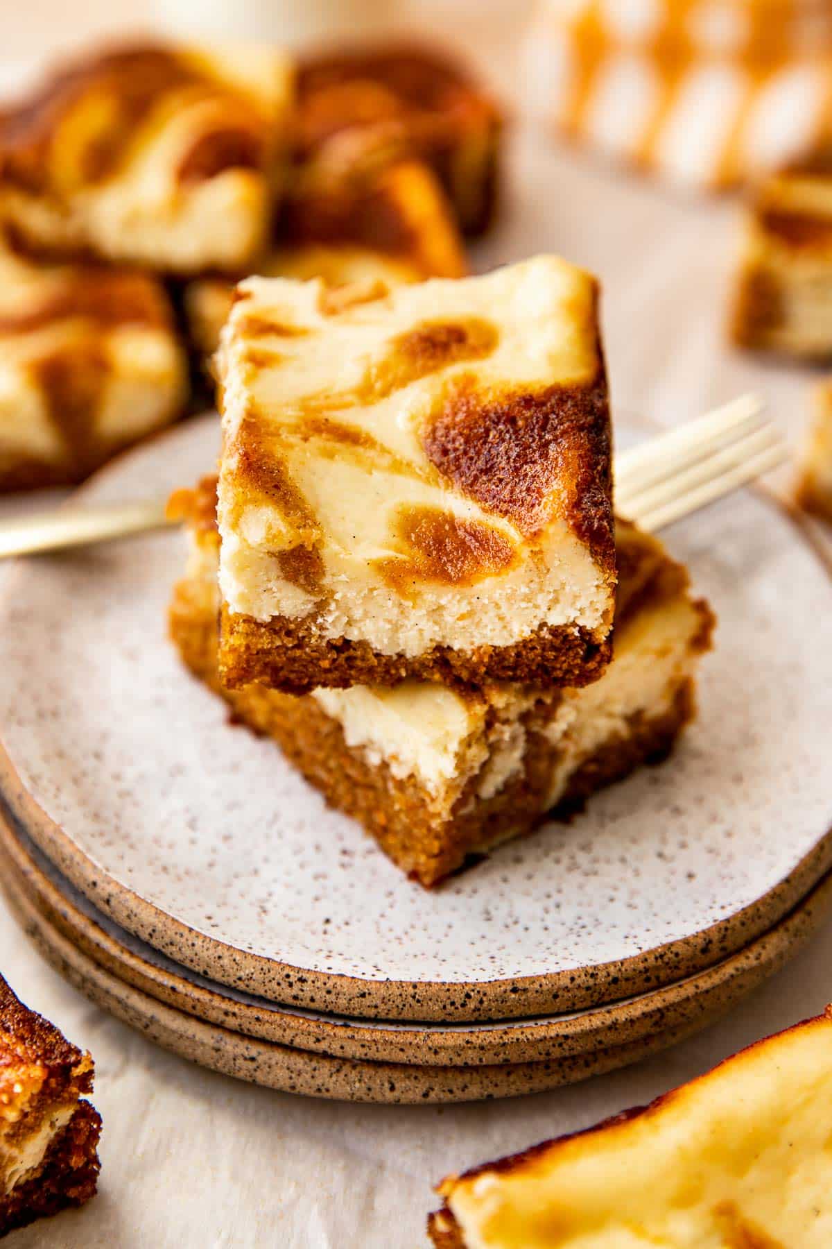 carrot cake cheesecake bars on white speckled plates. 