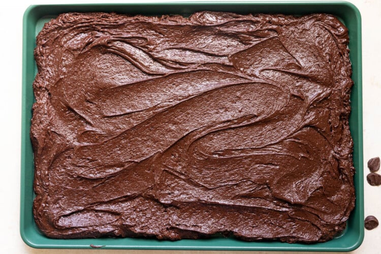 brownie batter spread out onto a green sheet pan.