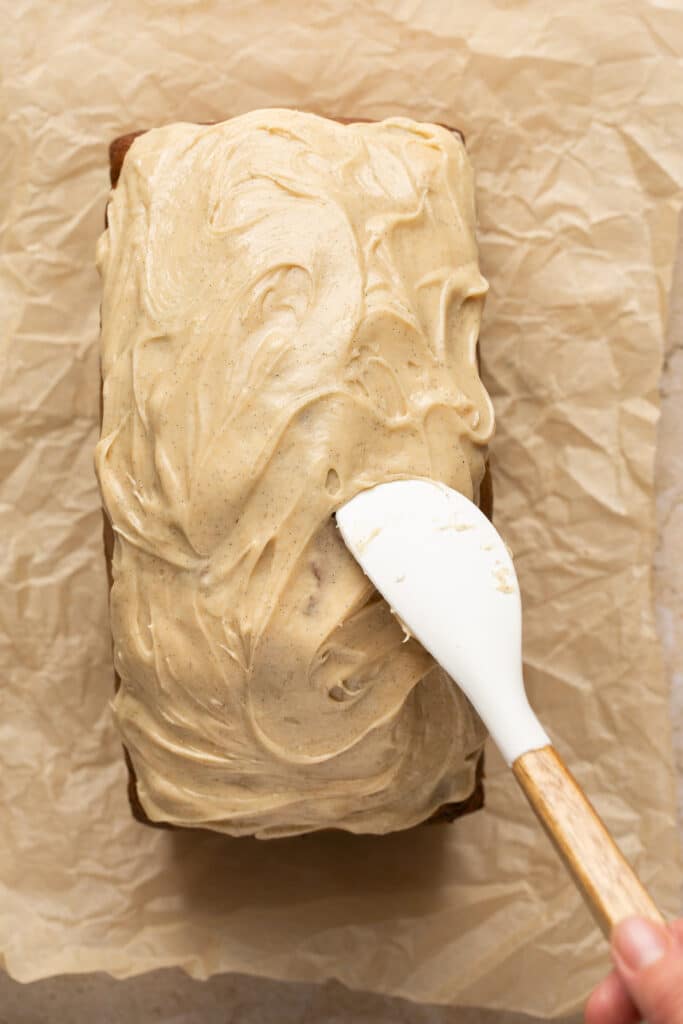brown butter frosting spread on top of zucchini banana bread with a white spatula. 