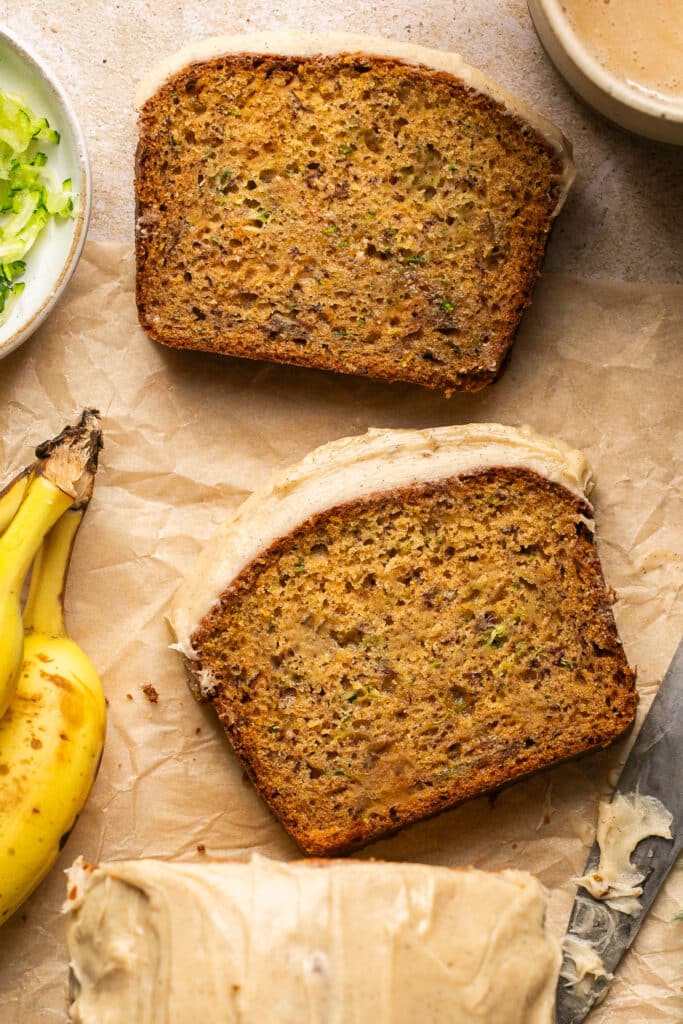zucchini banana bread sliced on parchment paper with frosting on top of the bread. 