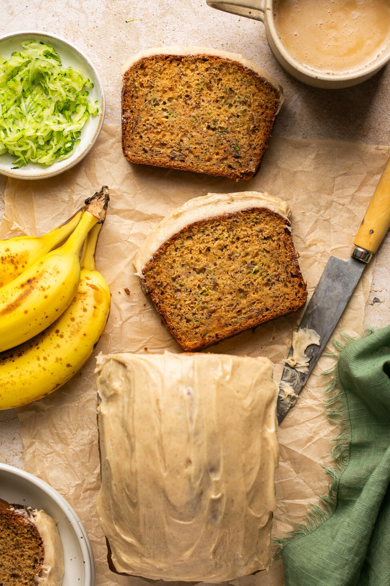 zucchini banana bread sliced on parchment paper with frosting on top of the bread. 