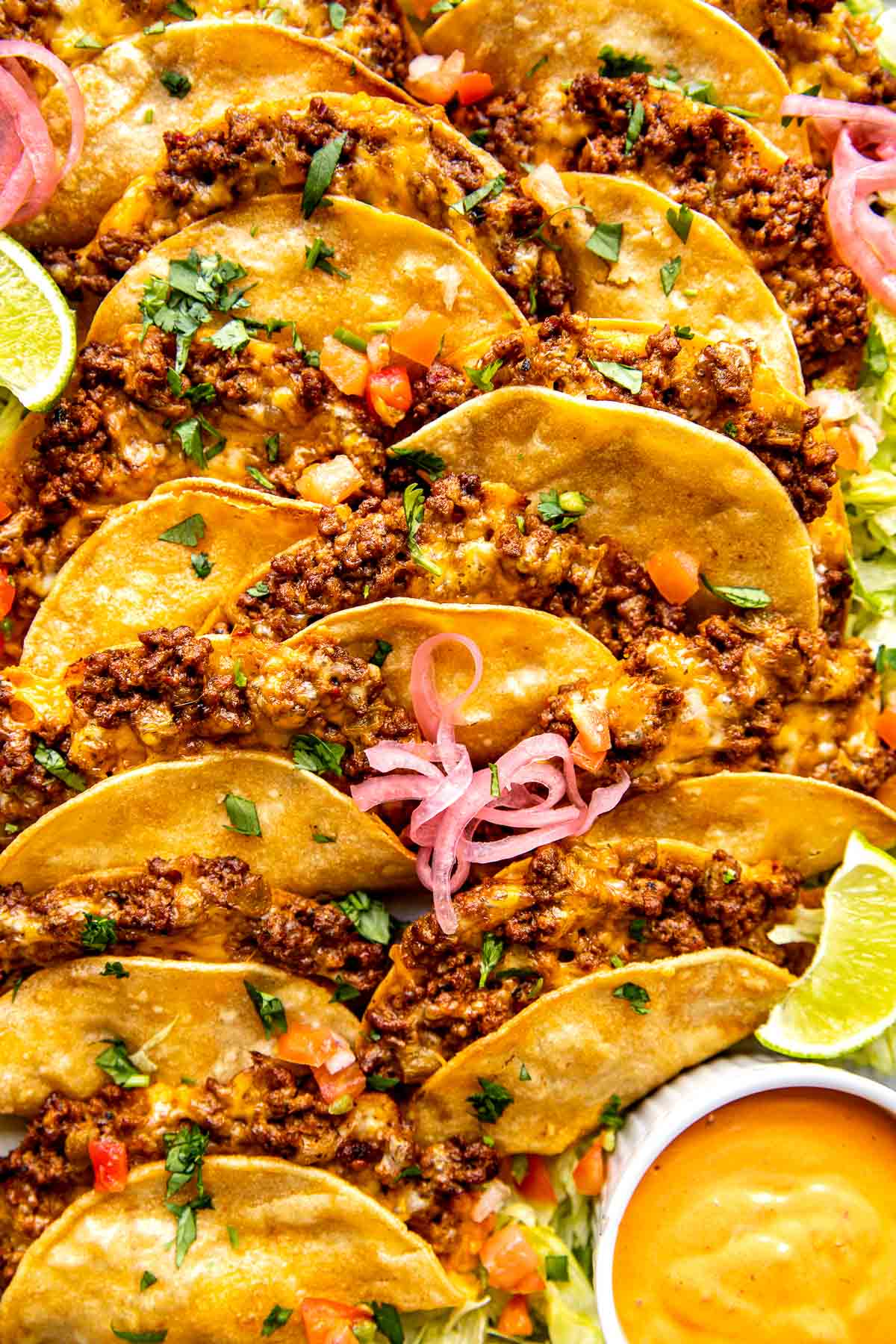 beef tacos garnished with cilantro, cheese, limes, and red onions. 