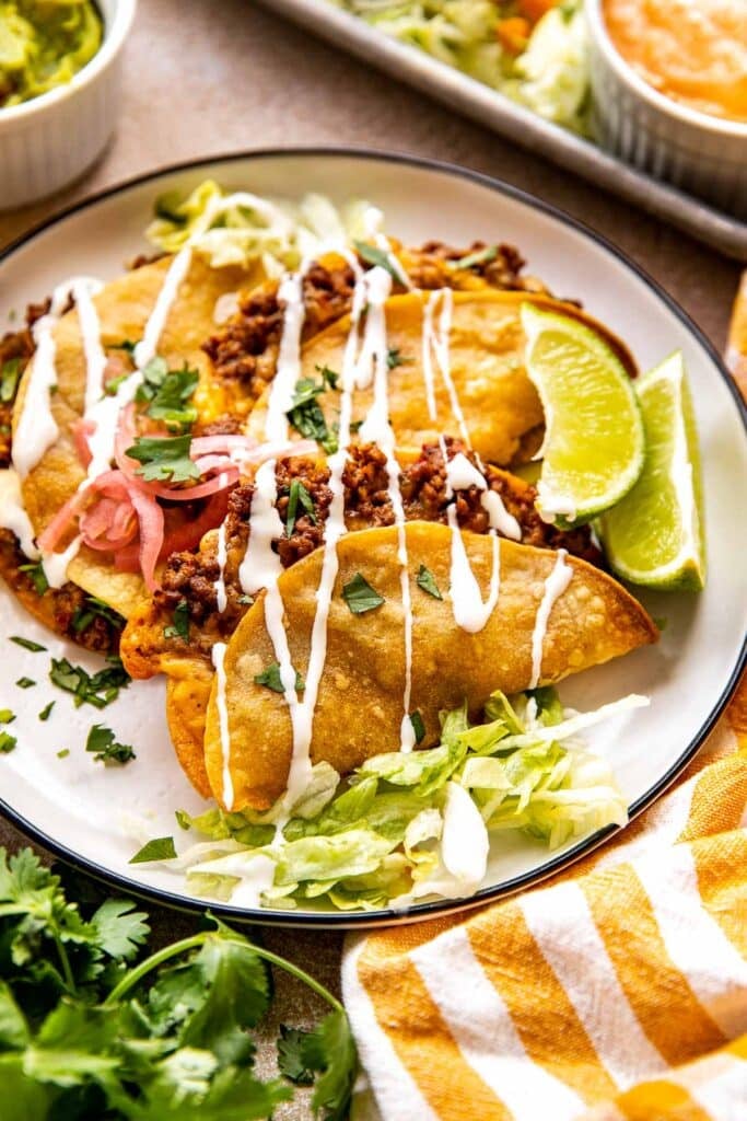 cheesy beef tacos on a white plate with sour cream drizzled over the tops. 