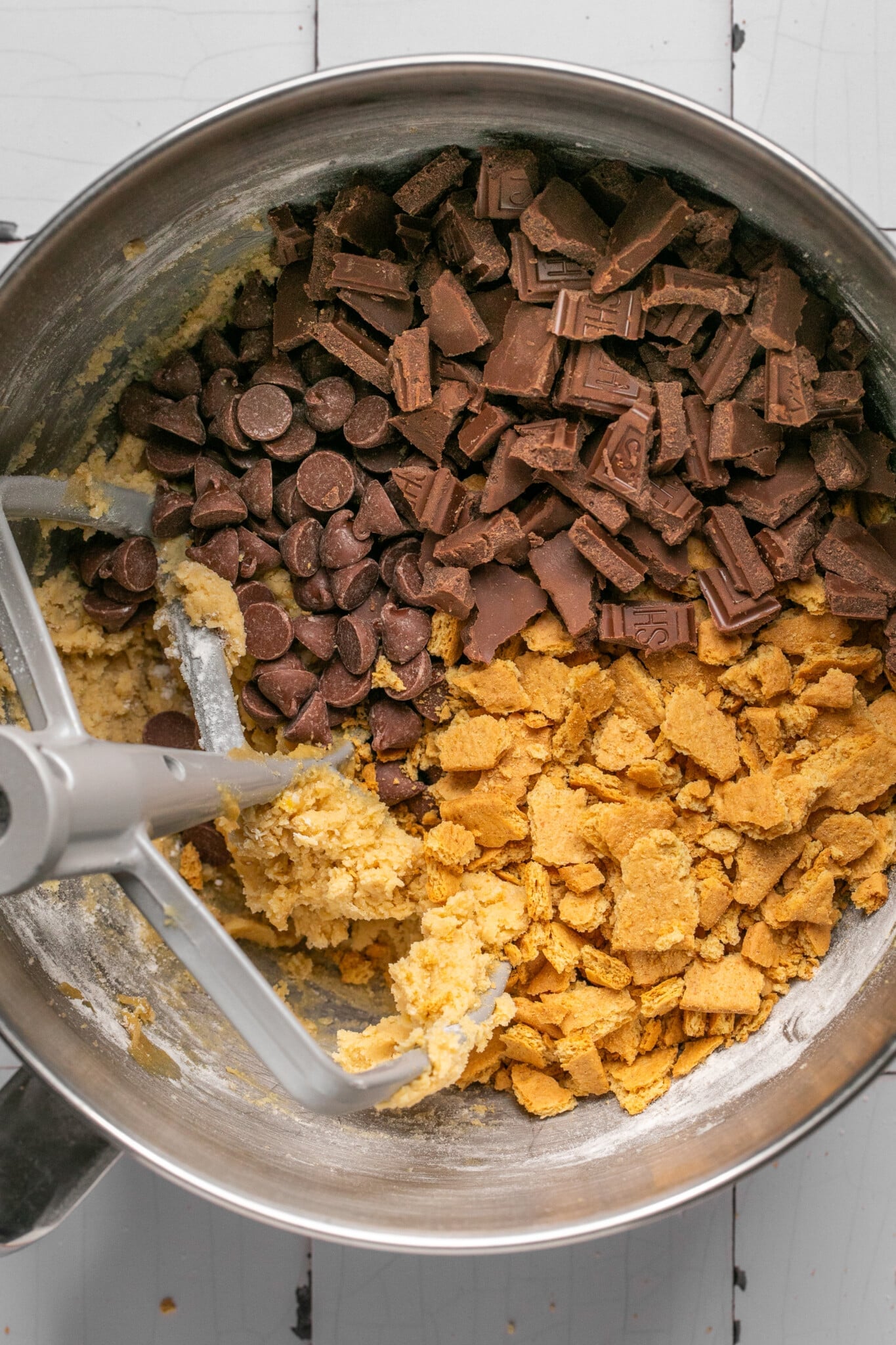 cookie dough in a mixing bowl with chocolate chips, Hershey's chocolate and graham crackers. 