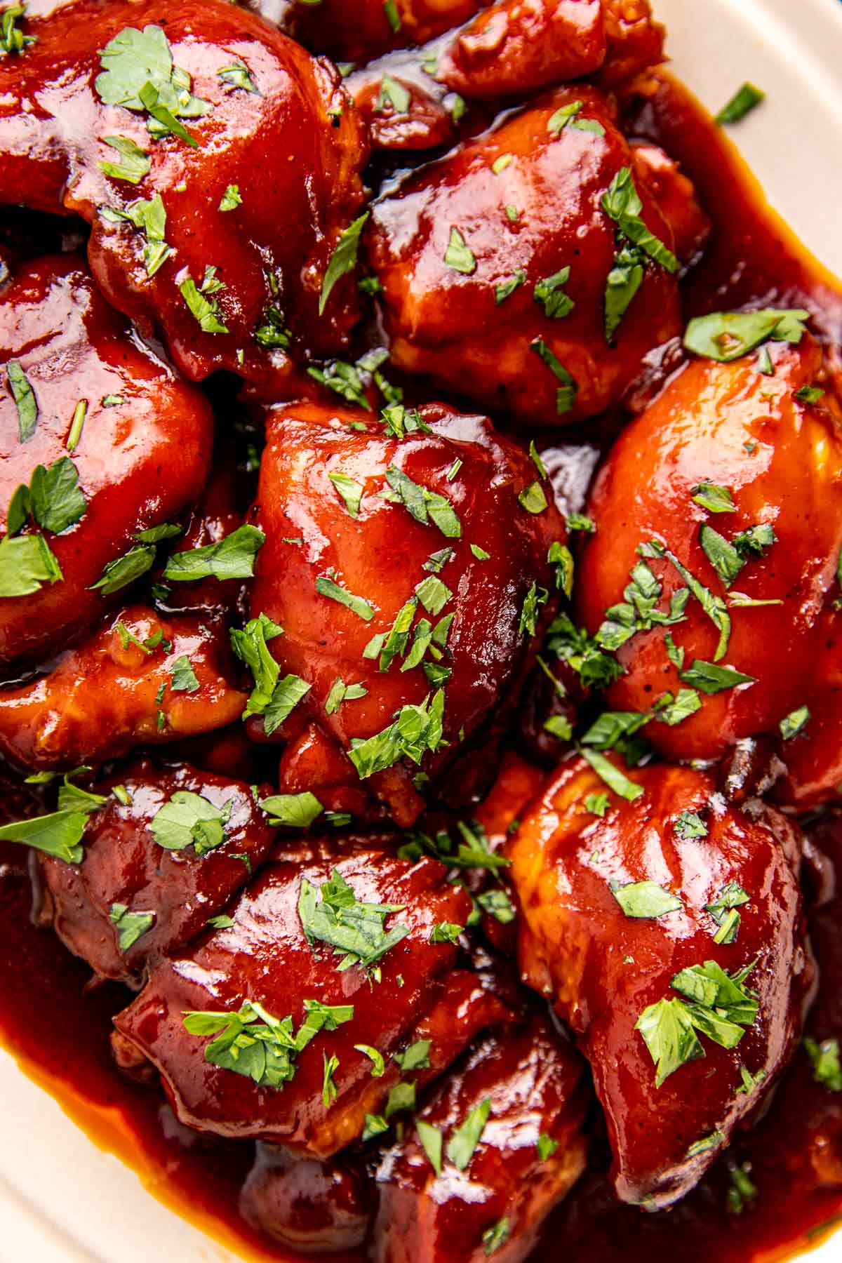 an up close image of chicken thighs with bbq sauce and parsley garnished on top.