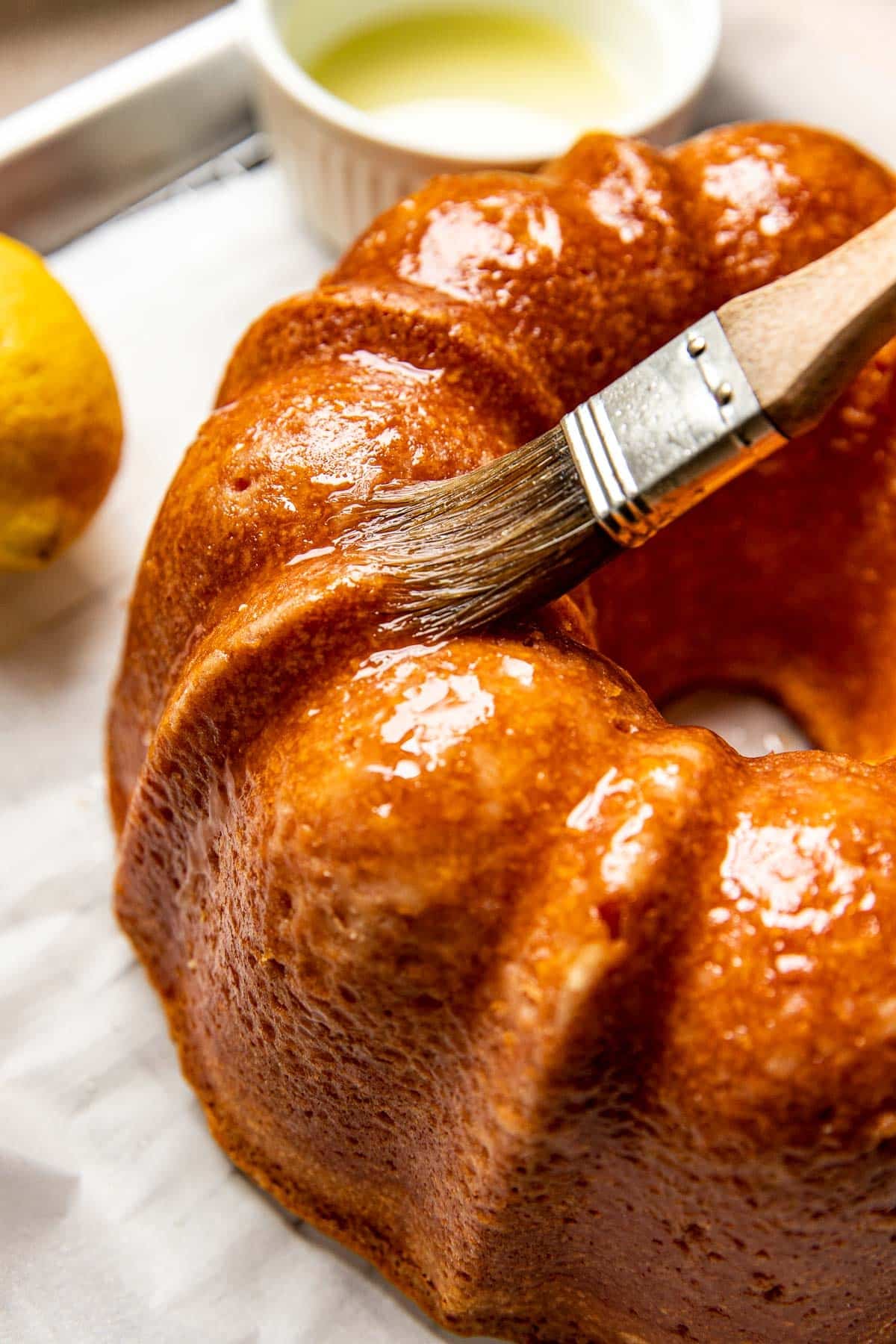 a brush on a bundt cake brushing on lemon syrup. 