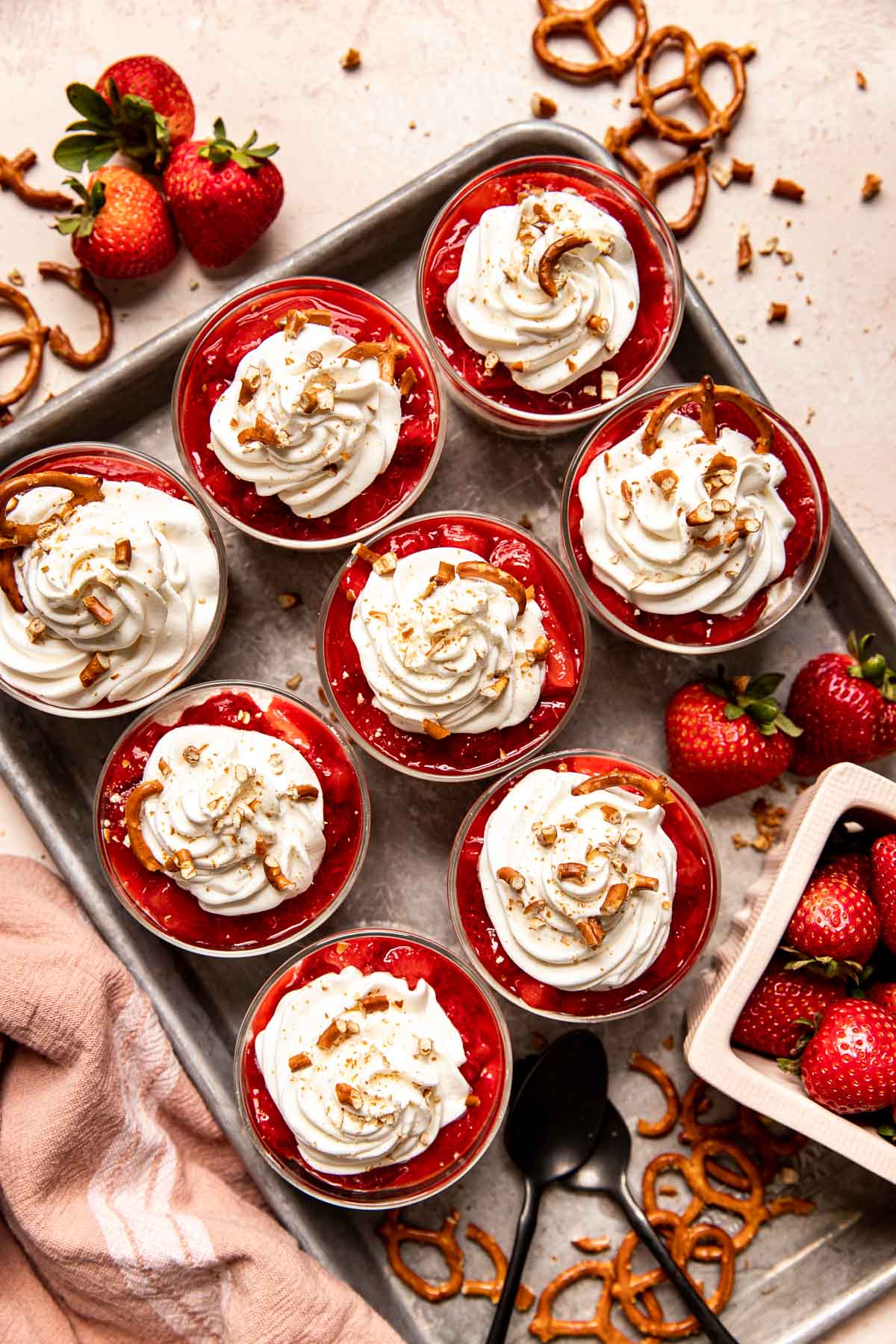 strawberry pretzel salads in parfait glasses topped with whipped cream and crushed pretzels.