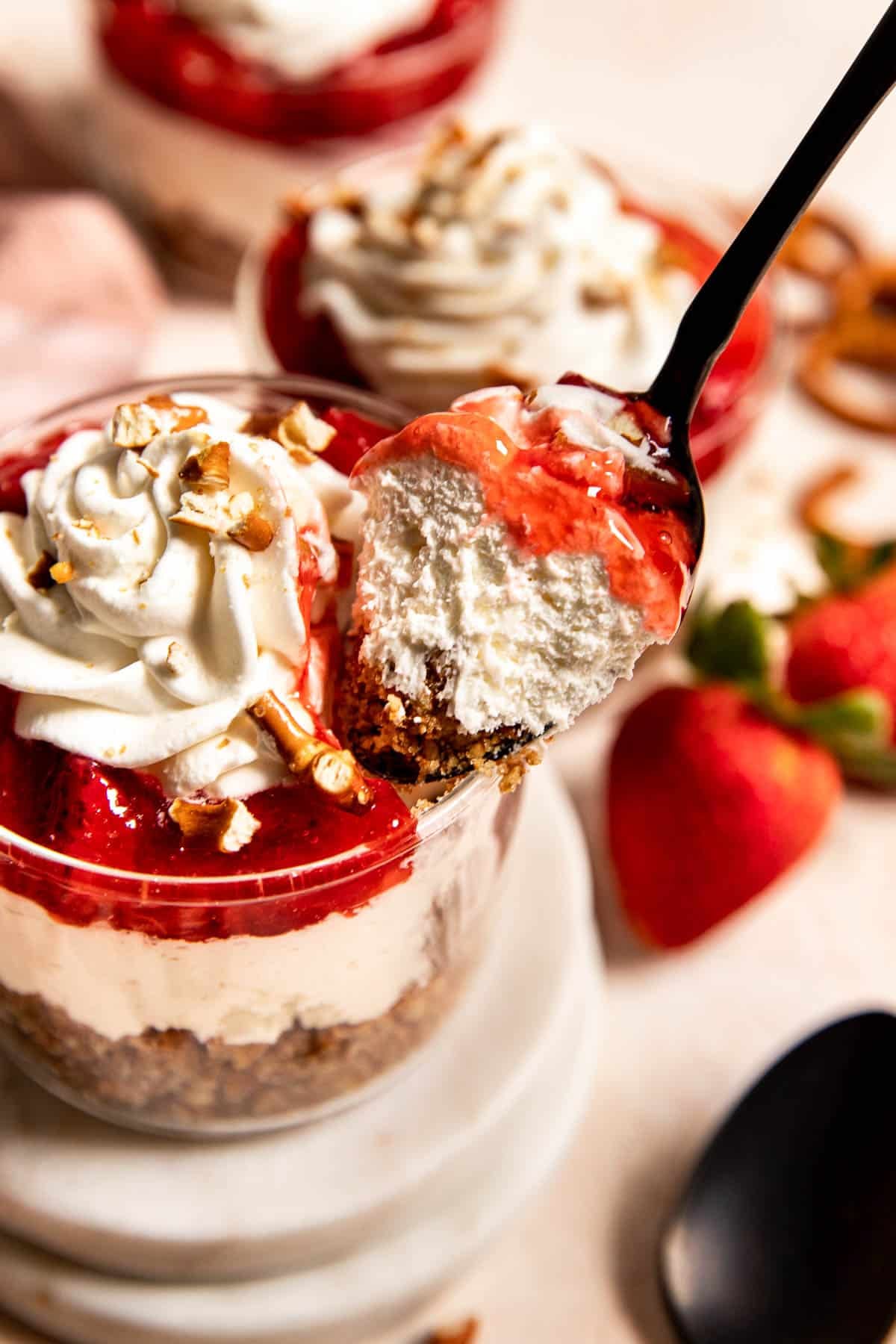 a black spoon taking a bite out of a strawberry pretzel salad parfait.
