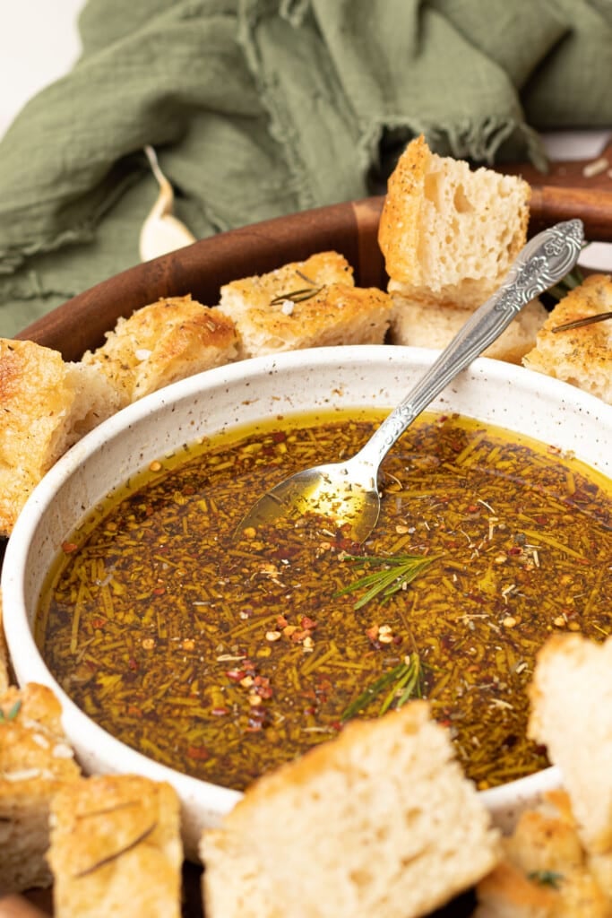 Bread dipping oil recipe in bowl with spoon and chunks of bread in serving bowl.