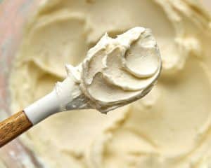 white spatula showing a small amount of vanilla frosting, with bowl of frosting in the background