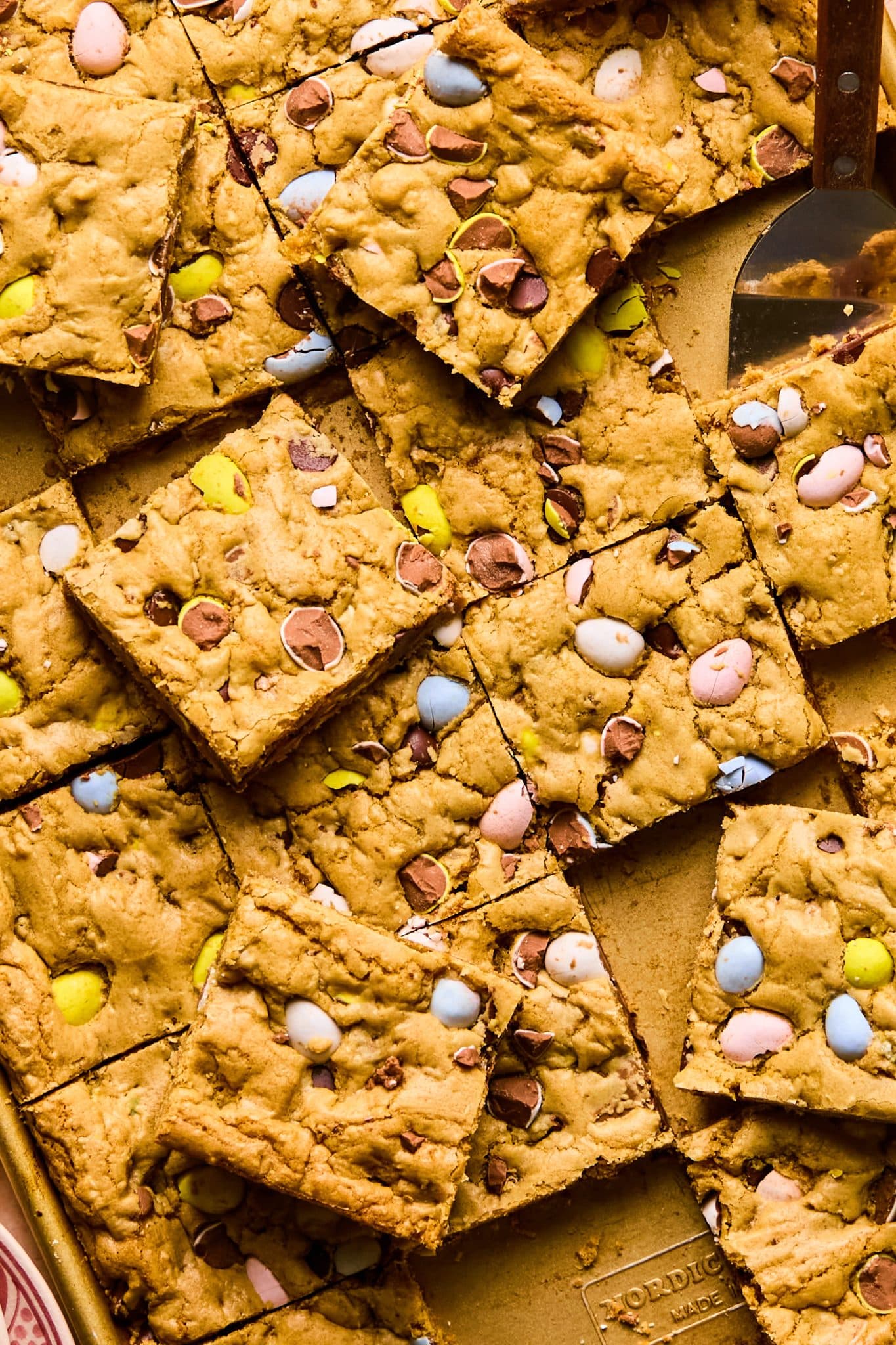 Close-up of overlapping Easter sheet pan cookie bars, highlighting the crackly tops and colorful cadbury eggs that are crushed up.