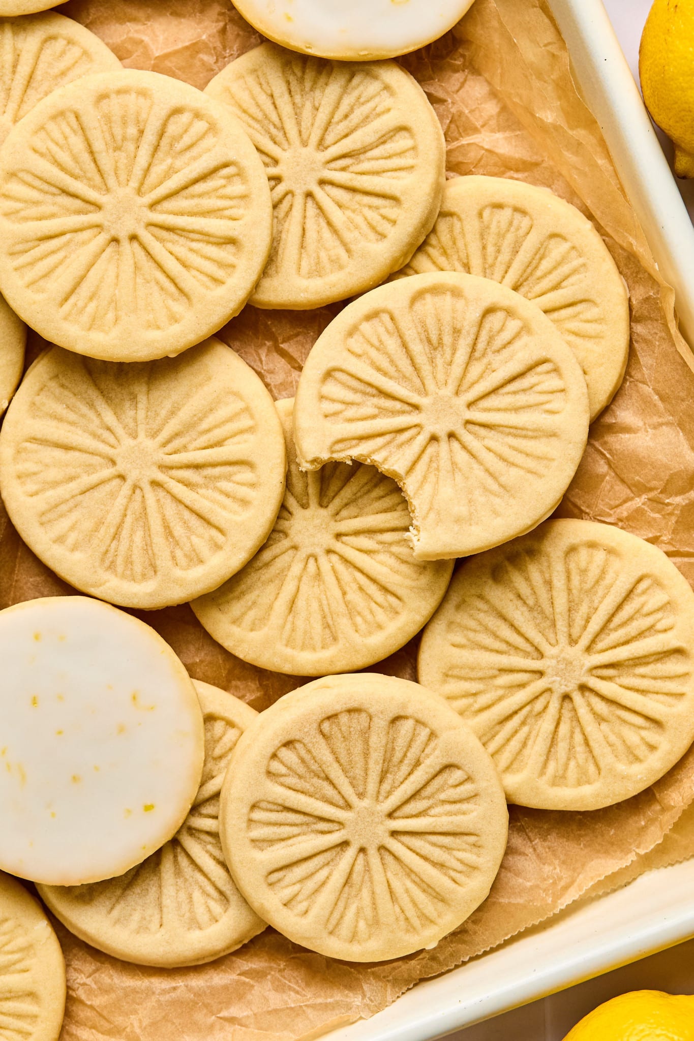 Lemonade cookies on parchment-lined baking sheet after they have finished setting from being dunked in the glaze. One cookie has a bite taken out of it and two of the cookies are showing the lemon glaze on the bottom.