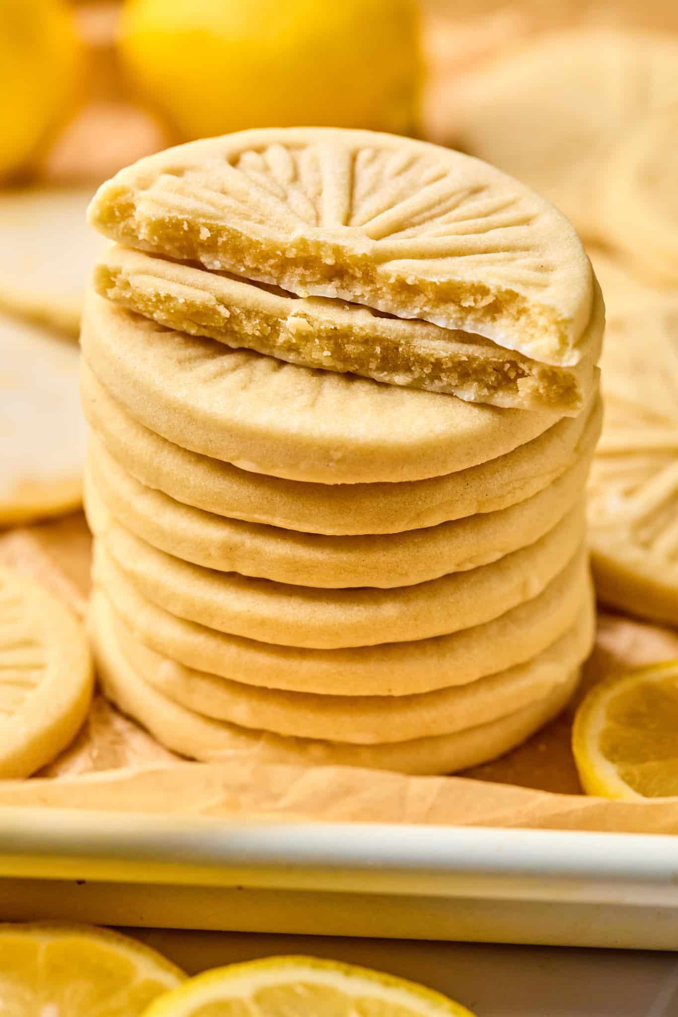Stack of copycat girl scout lemonade cookies on parchment-lined baking sheet. The top two cookies are cut in half so you can see the middle of the cookie.