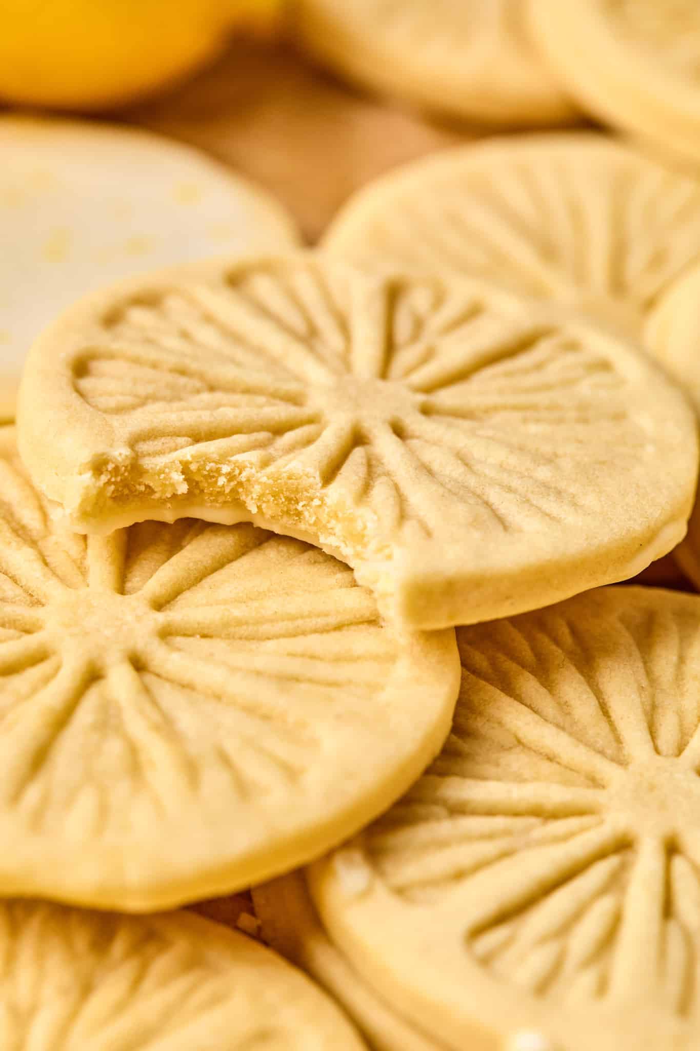 Lemonade cookies piled on top of each other and the top cookie has a bite taken out of it showing the inside of the cookie.