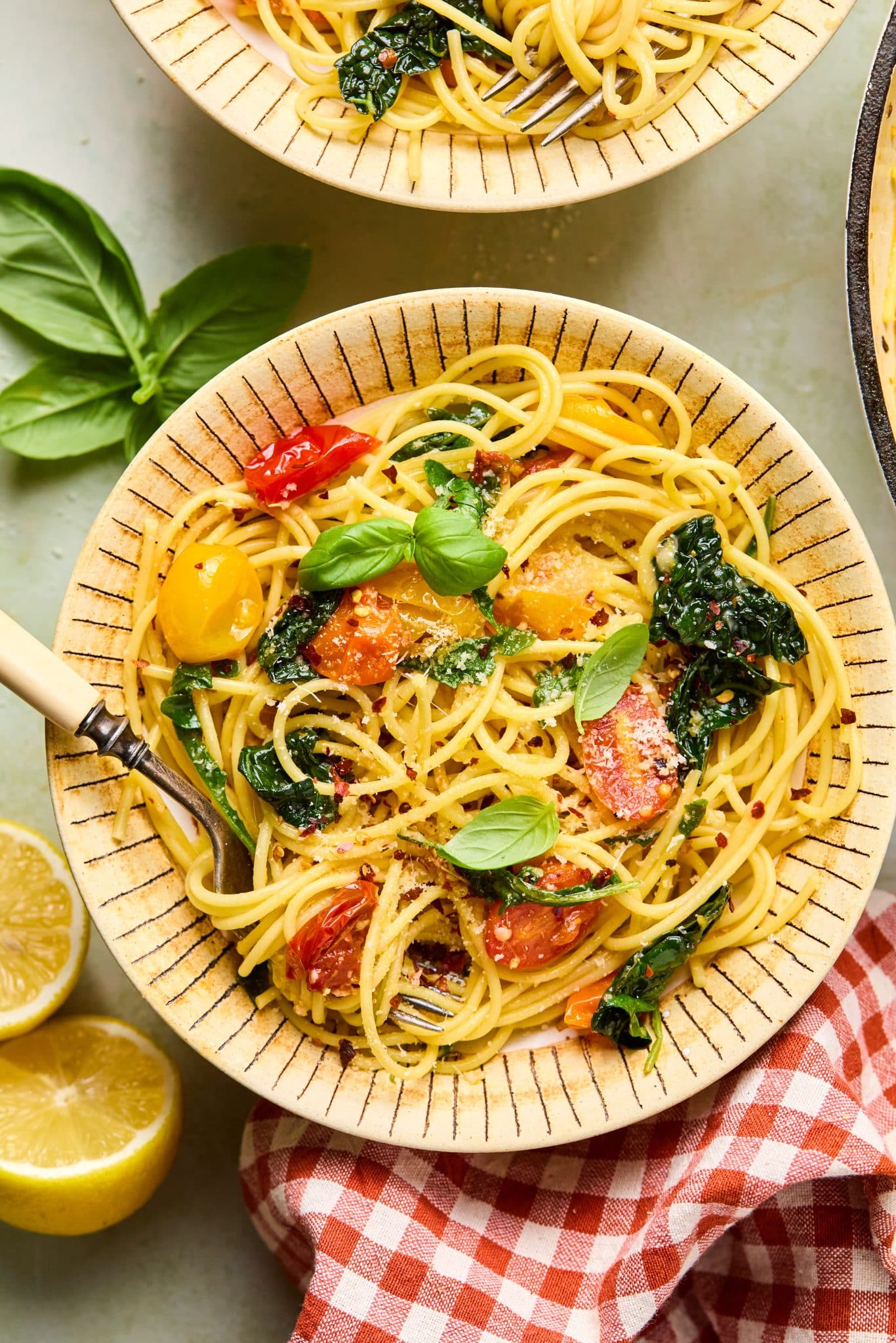 A warm, rustic bowl filled with golden spaghetti, blistered cherry tomatoes, wilted kale, and fresh basil, topped with grated Parmesan and red pepper flakes.