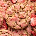 A close-up overhead shot of strawberry-glazed oatmeal cookies, showing their craggy texture and pink glaze. Freeze-dried strawberry slices are scattered among the cookies.